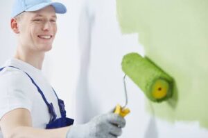 Happy and young man is painting a wall green